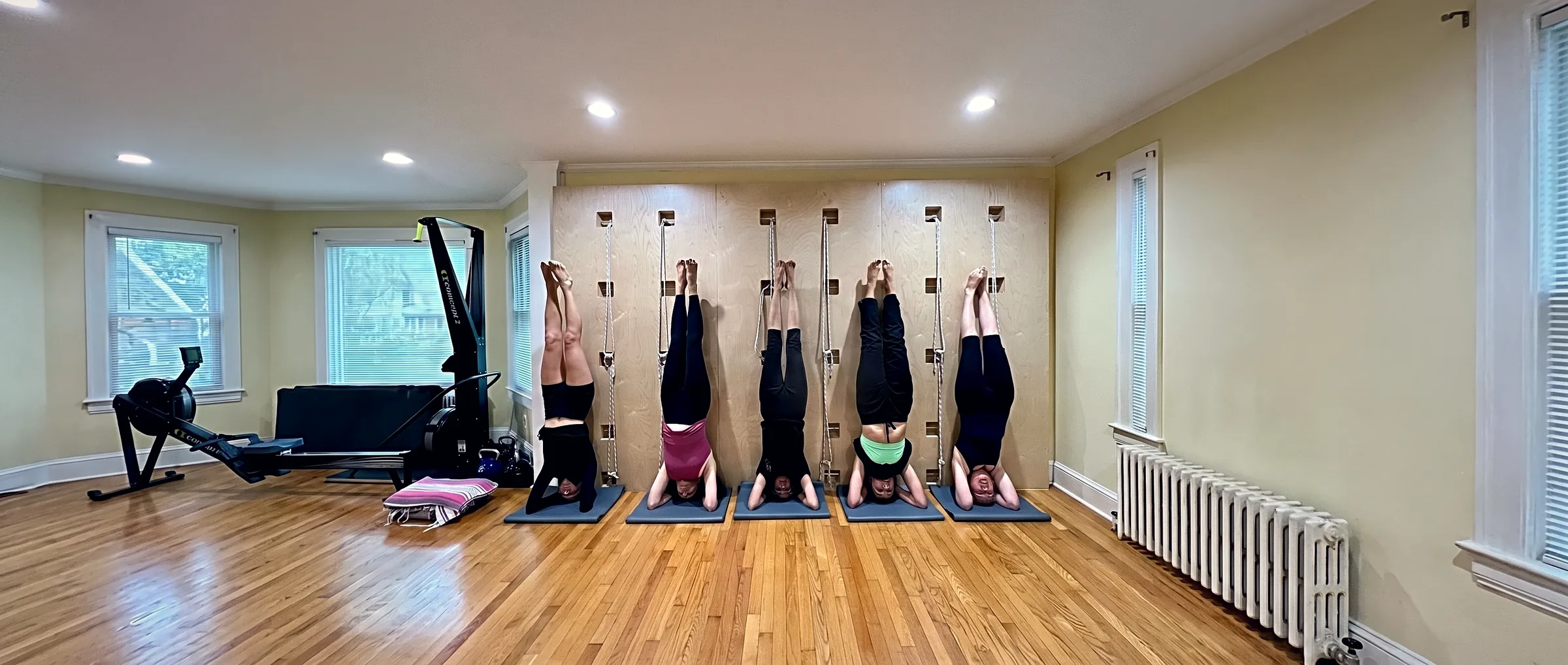 Five members practising a supported headstand side by side against the studio’s rope wall